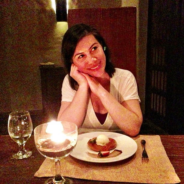 the lady in a white shirt is sitting at a table with wine