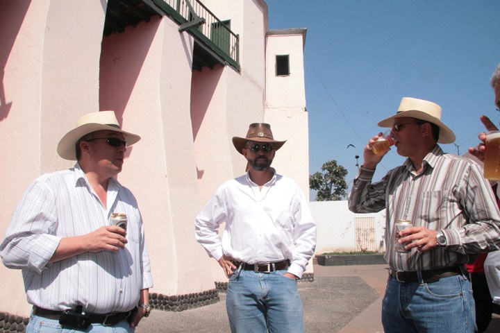 three men in hats are standing together, one holding two beers