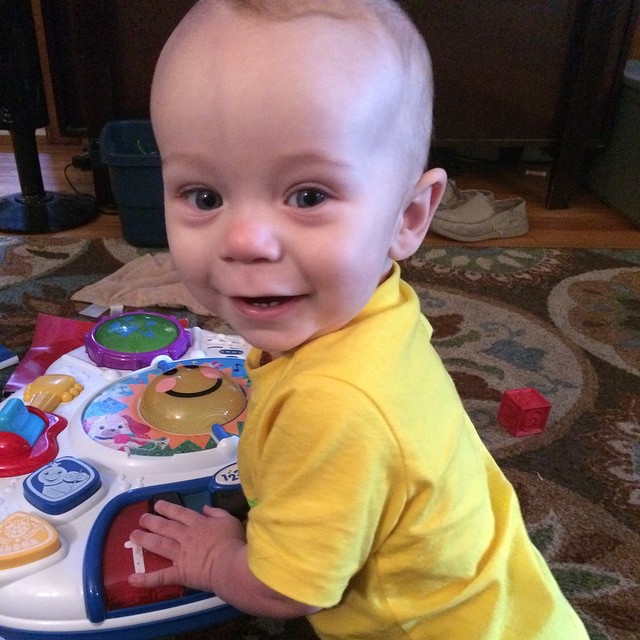 a baby smiling next to an activity play table