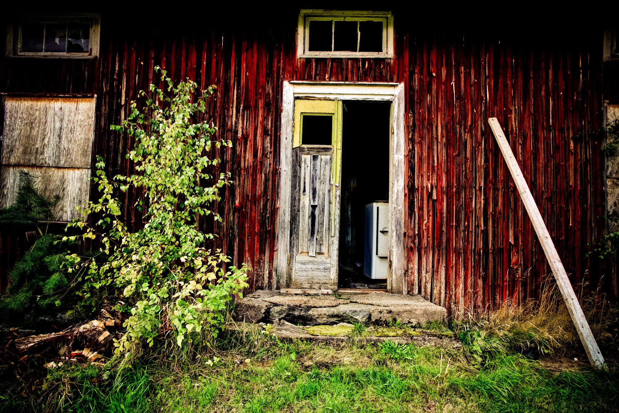 an old red barn with green grass and a tree