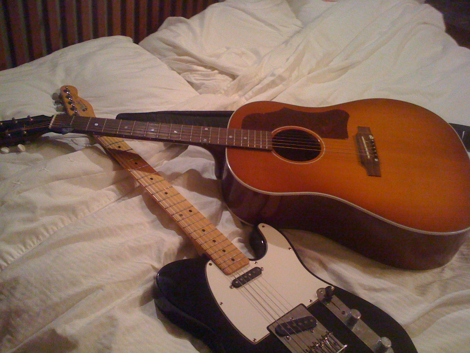 three guitars laying on a bed, one of which is a ukulele and one of which is a ukulele
