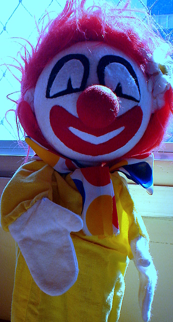 a clown - like stuffed animal is posed in the sunlight
