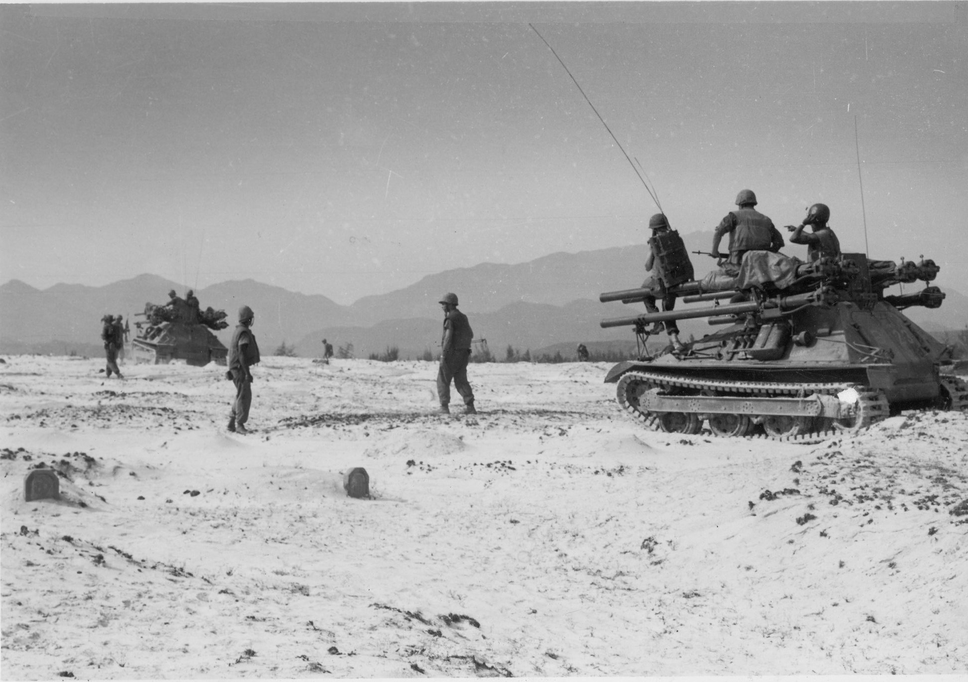 some men stand near military vehicles in the sand