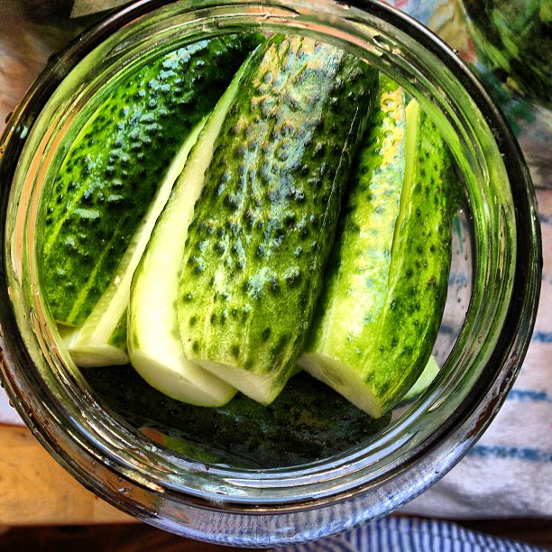 a glass jar full of cucumbers next to two others