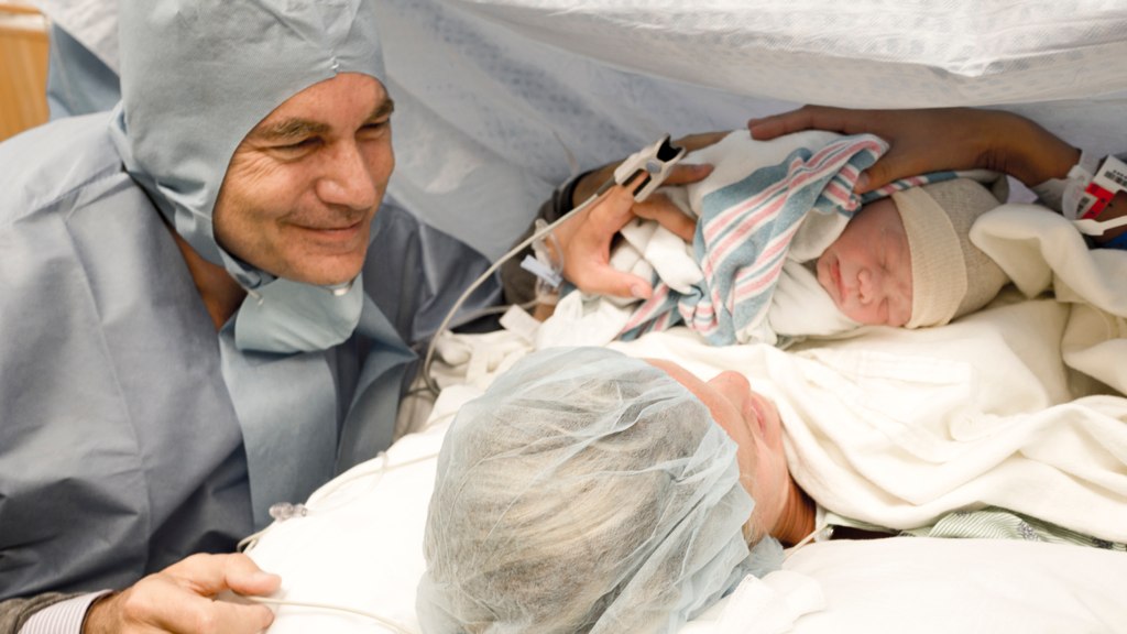 two men dressed in hospital clothes examine a baby