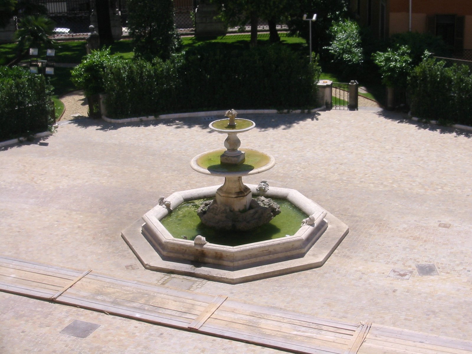 an aerial view of a water fountain surrounded by hedges and trees