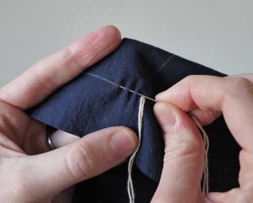 two hands pulling together yarn that is on the end of a cloth bag