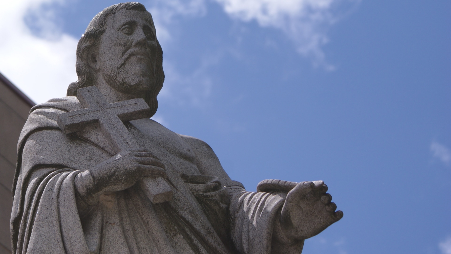 a statue holding a cross in front of a blue sky