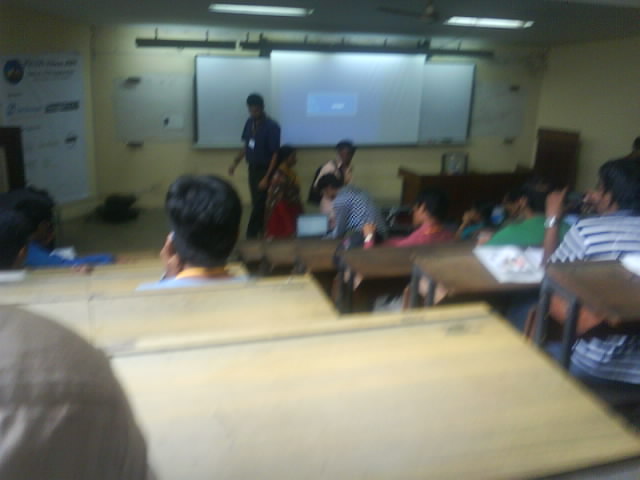 a lecture room is full of children, sitting at desks with a projector screen