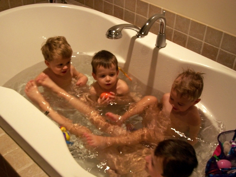 three s are in the bathtub while one plays with an orange