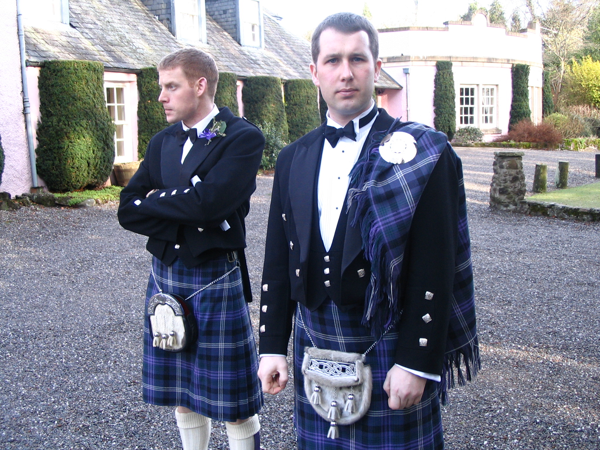 two men are wearing kilts outside, one is in a blue suit and the other in a white shirt