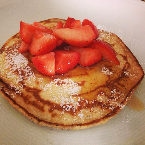 a white plate topped with pancakes covered in powdered sugar and sliced strawberries