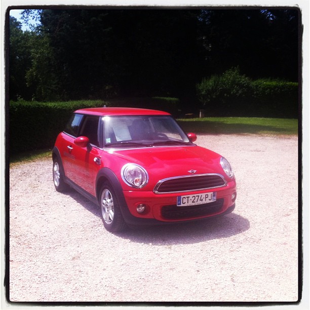 the mini is parked in the gravel near bushes