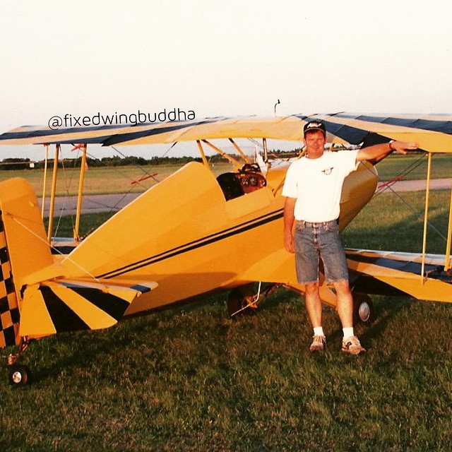 a man in white shirt standing in front of a yellow airplane