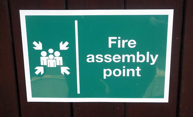 a green fire assembly point sign mounted to a wood wall