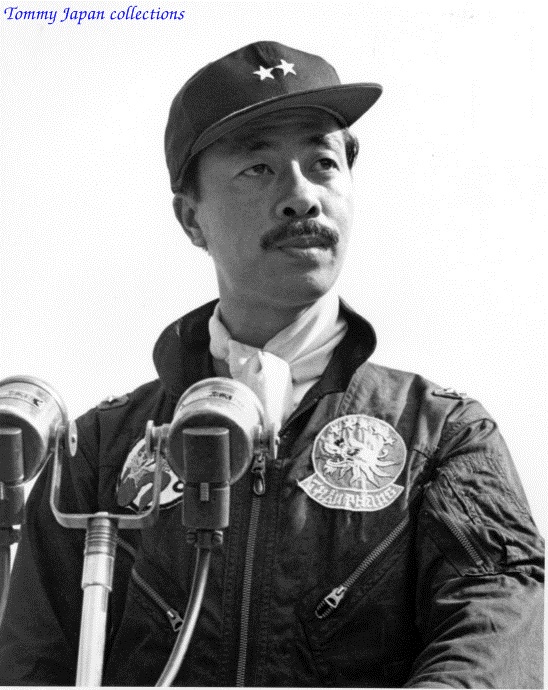 a man that is wearing a hat and standing in front of microphones
