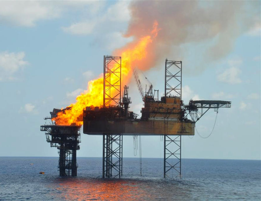 the view from water shows an oil rig with the fire coming out