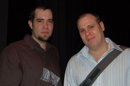two males pose for the camera with a dark background