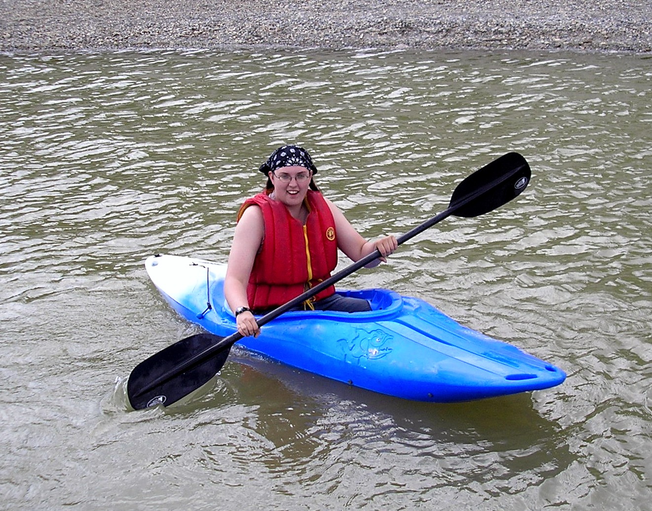 a woman in a red and blue kayak smiles as she stands in shallow water