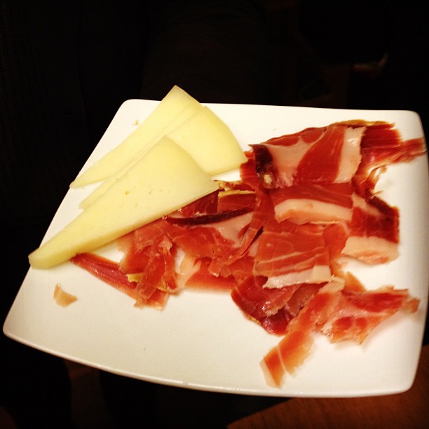 white plate with meats and cheese on it, sitting on wooden table