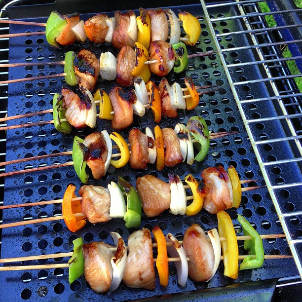several skewers of meat and vegetable sit on a grill