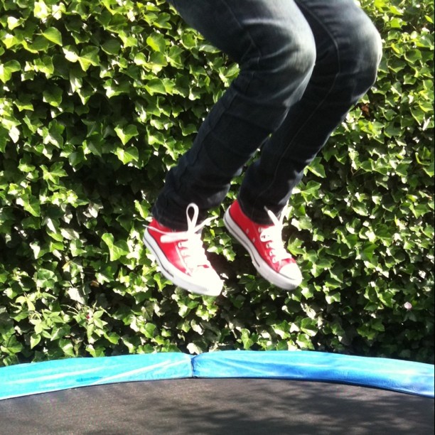 man jumping over a trampoline in red sneakers