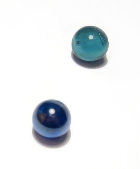 two blue beads sitting on a white surface