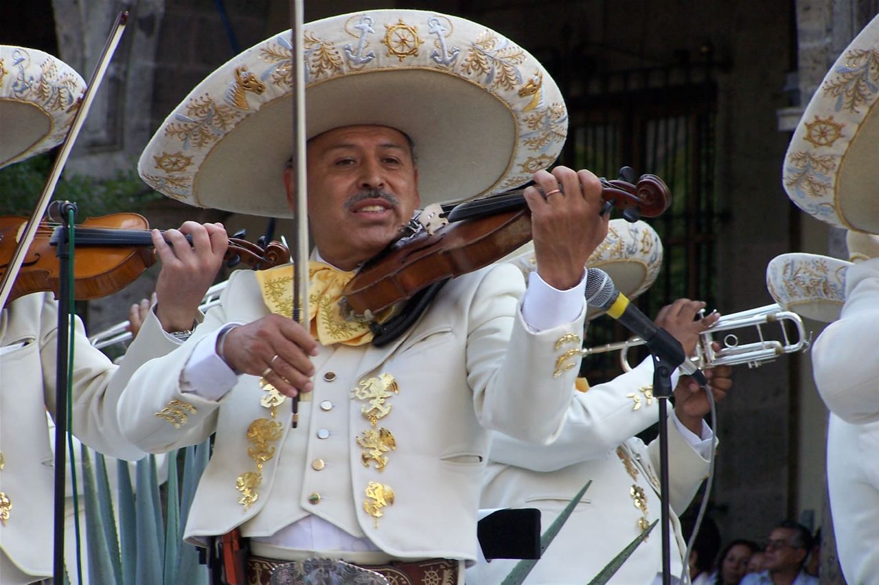 a man in white clothing and hat holding a violin