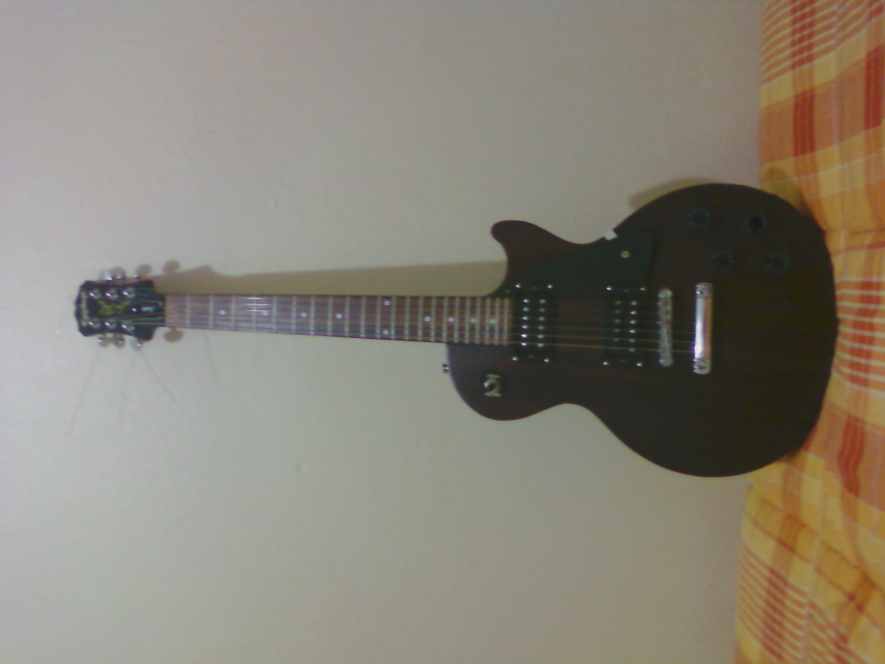 a black electric guitar resting against a wall