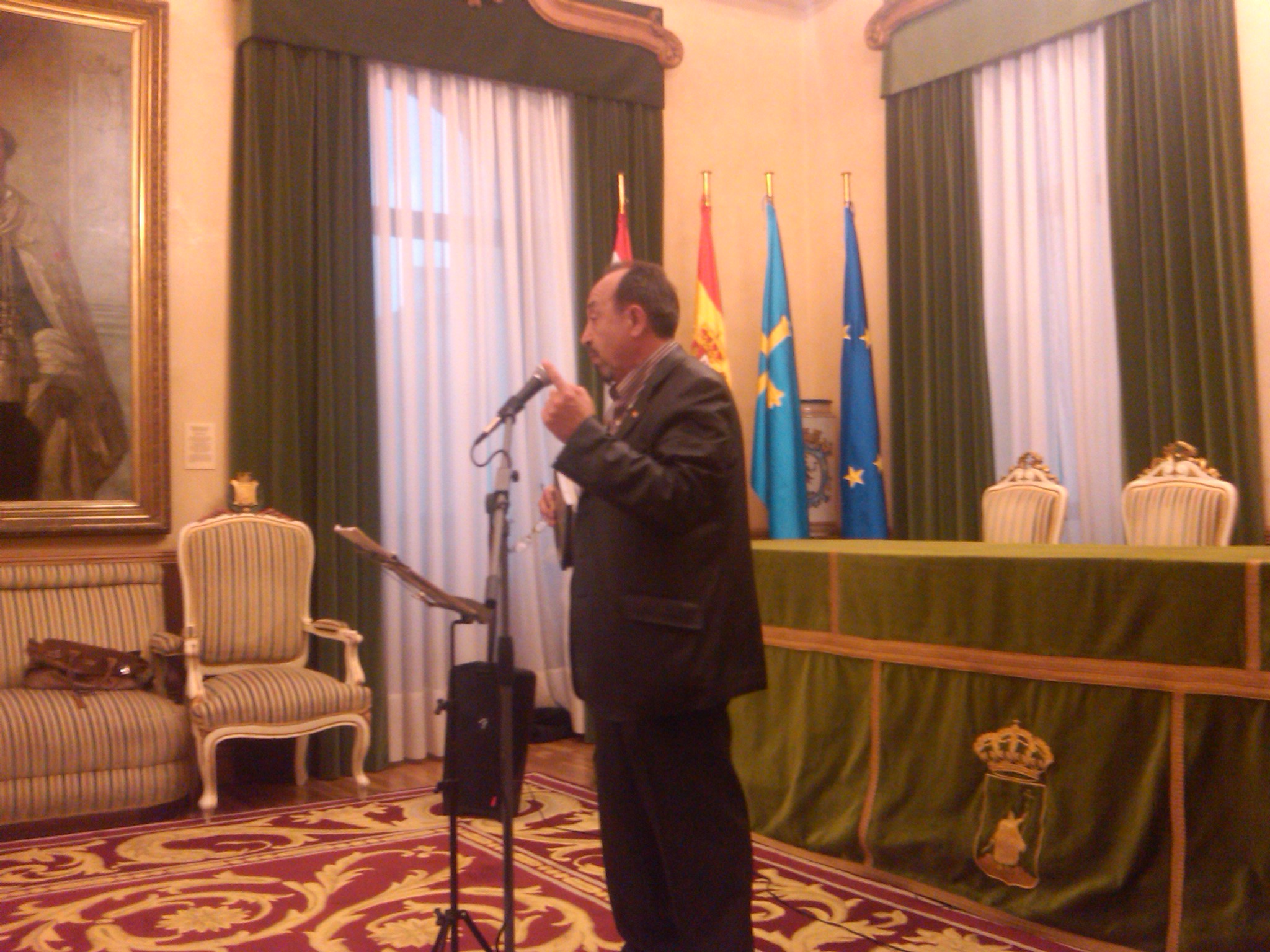 man in suit giving speech next to flags