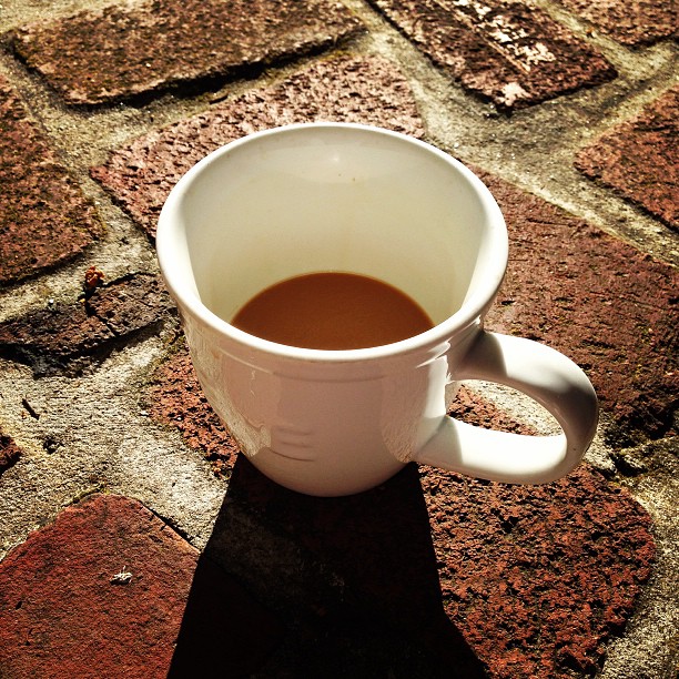 a mug of coffee sitting on top of a brick floor