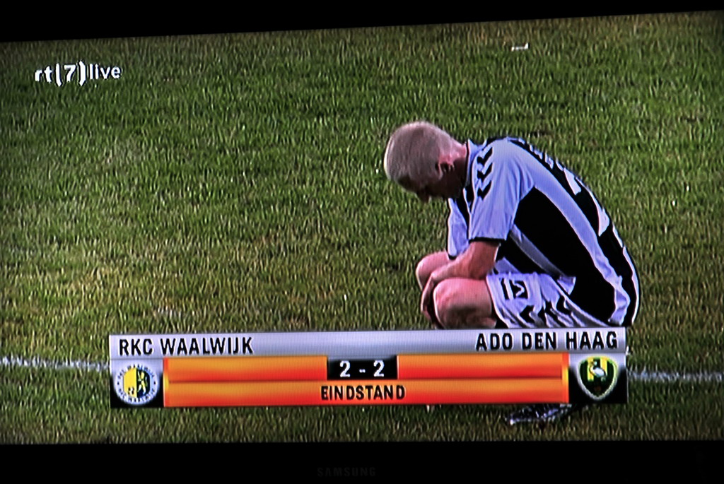 a soccer player is sitting on the grass by the scoreboard