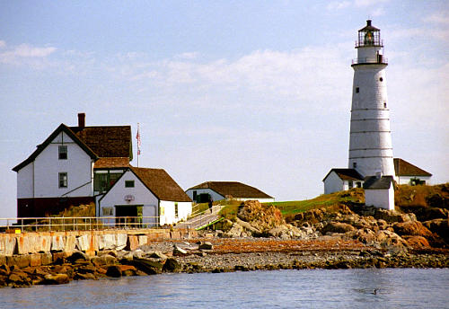 the white lighthouse on top of a hill next to water