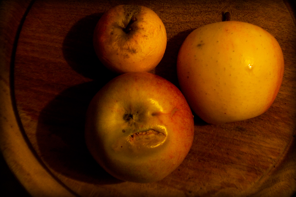 three apples and one orange sit on a wooden tray