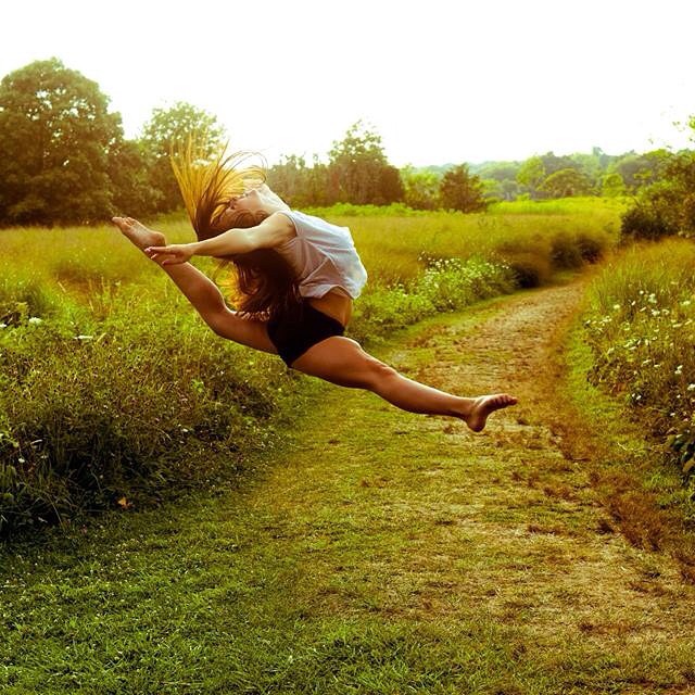 girl with leg extended jumping and grass area around