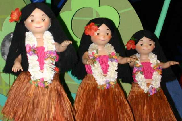 three dolls, including one girl with flowers in her hair, are posed together