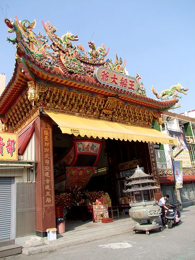 a asian temple on the side of the road with people milling around