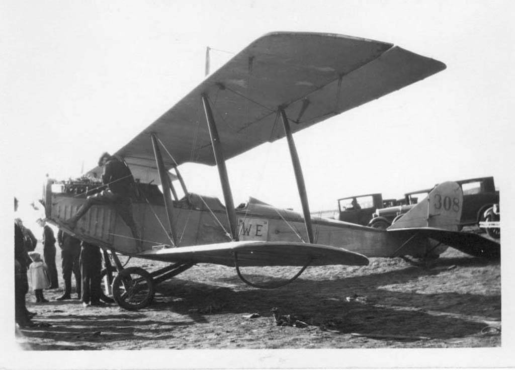 an old plane sits in the dirt as people are around it