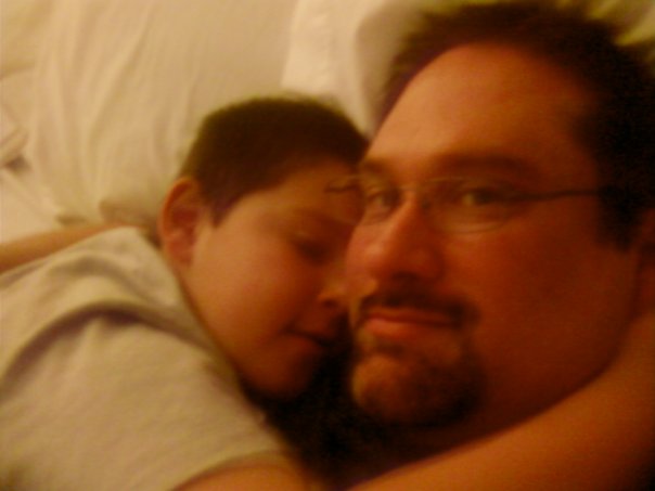 a man laying next to his child on top of bed