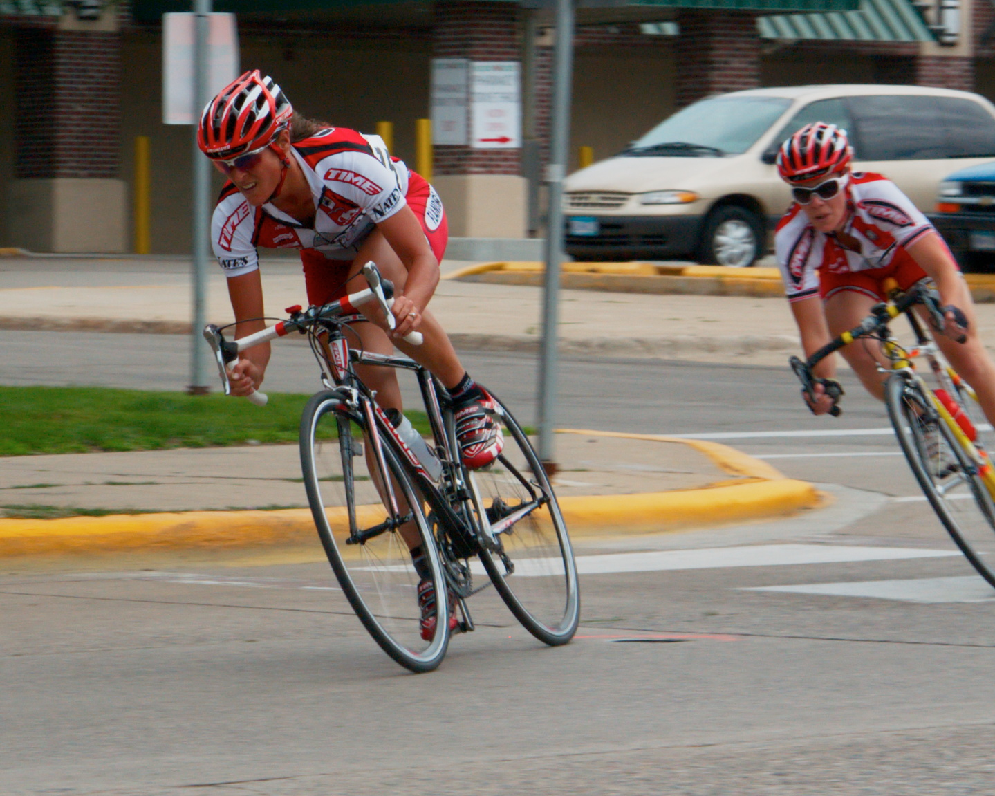 two people riding bikes on a road next to a sidewalk