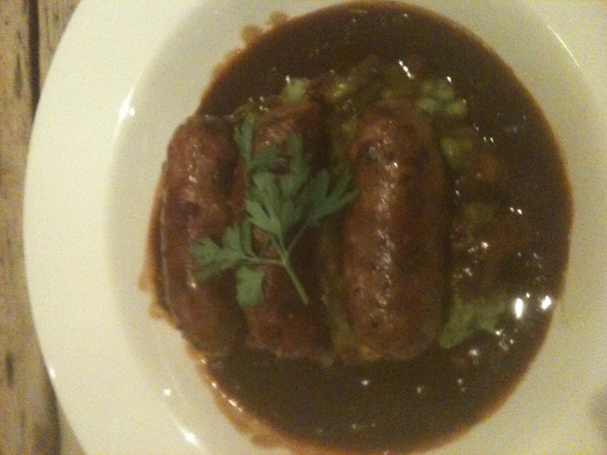 a plate with two sausages in gravy on top of it
