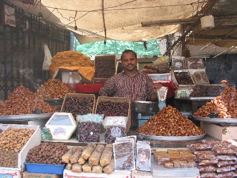 man standing behind a stand that has many different kinds of foods