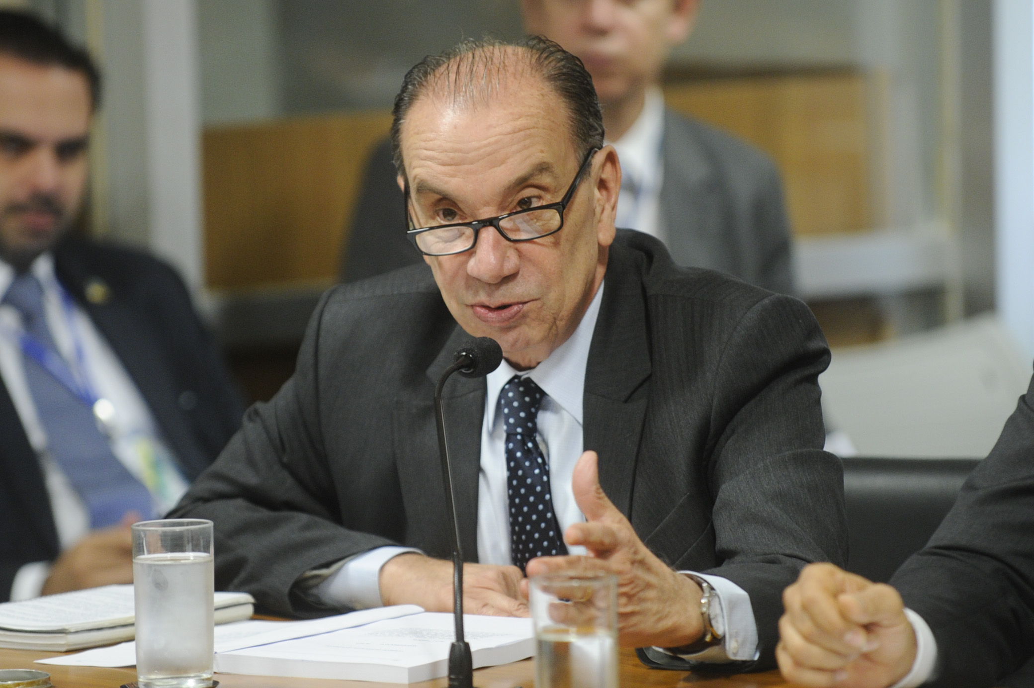 a man with glasses and a tie in front of him giving a speech