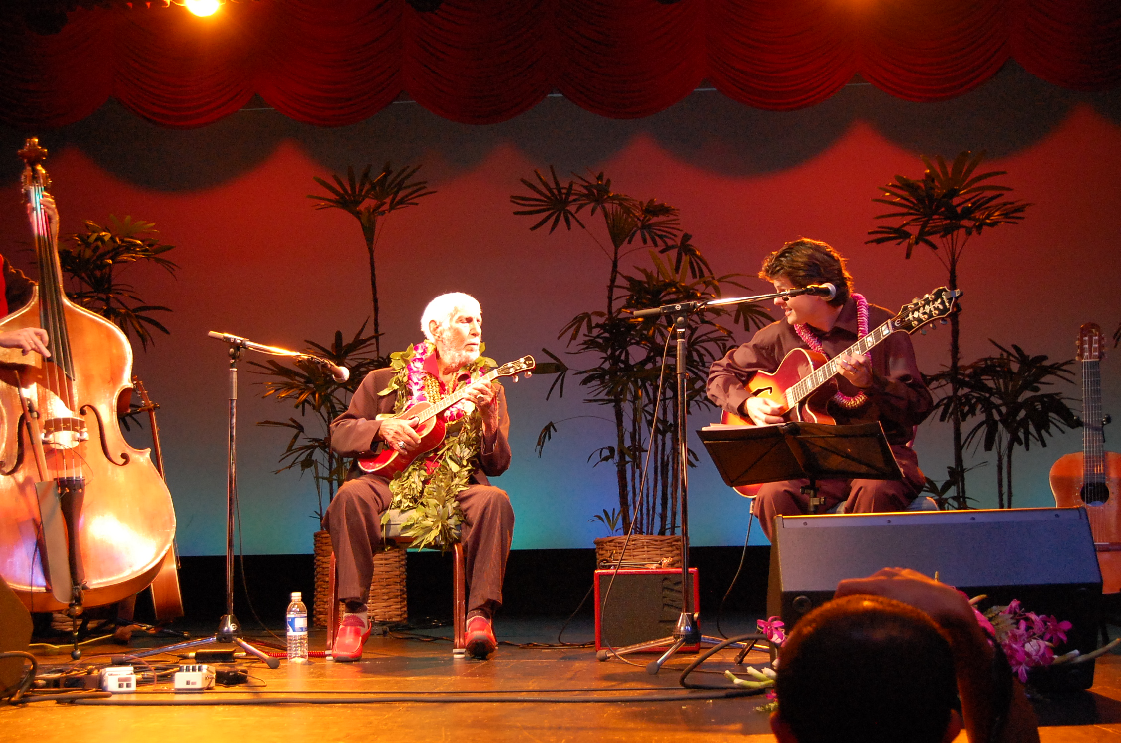 three people on stage playing music, one has an acoustic instrument