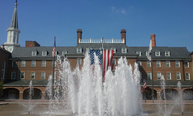 a fire hydrant with water shooting up and flags flying in the background