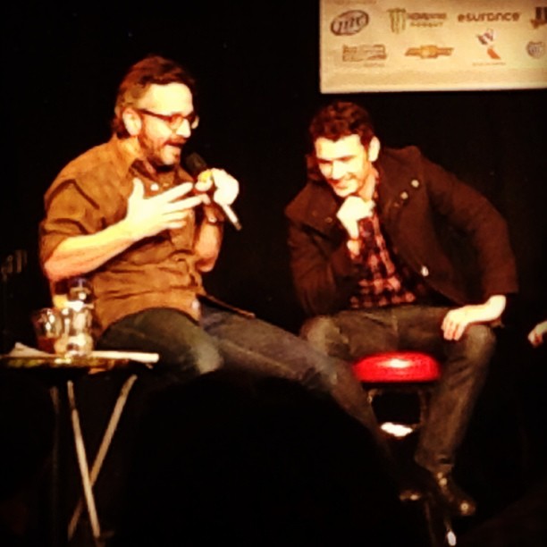two men are sitting and talking on stage