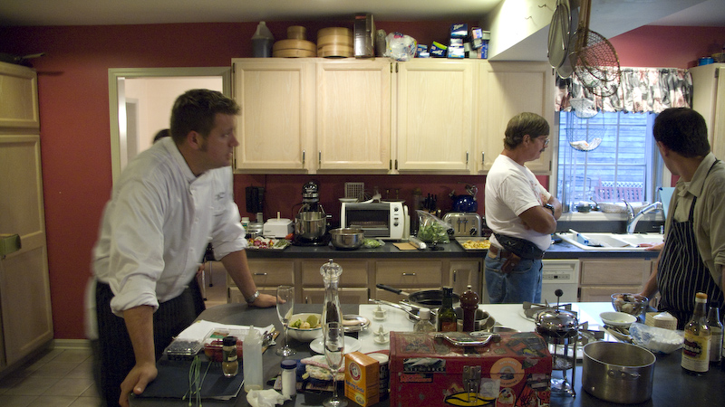 men are standing around the kitchen in a kitchen