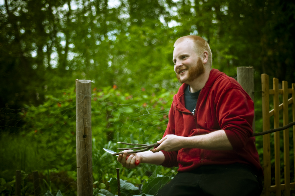 man holding some scissors while smiling in front of a fence
