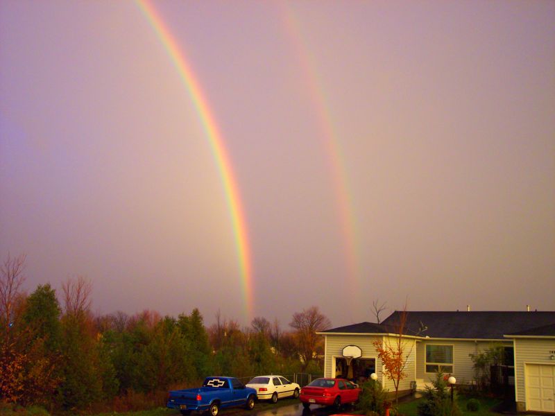 a rainbow over two house on a very cloudy day