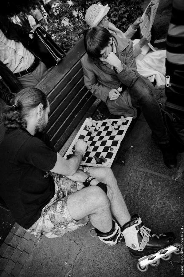 two people playing chess on the sidewalk in front of a bench